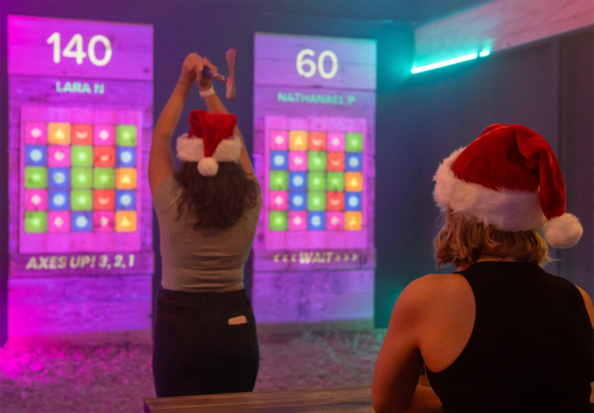 Colleagues in Santa hats throwing axes at glowing digital targets