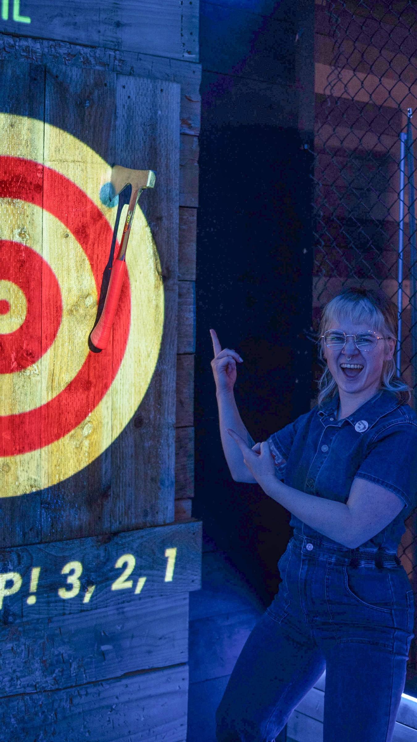 Woman pointing excitedly at her axe stuck in the bullseye