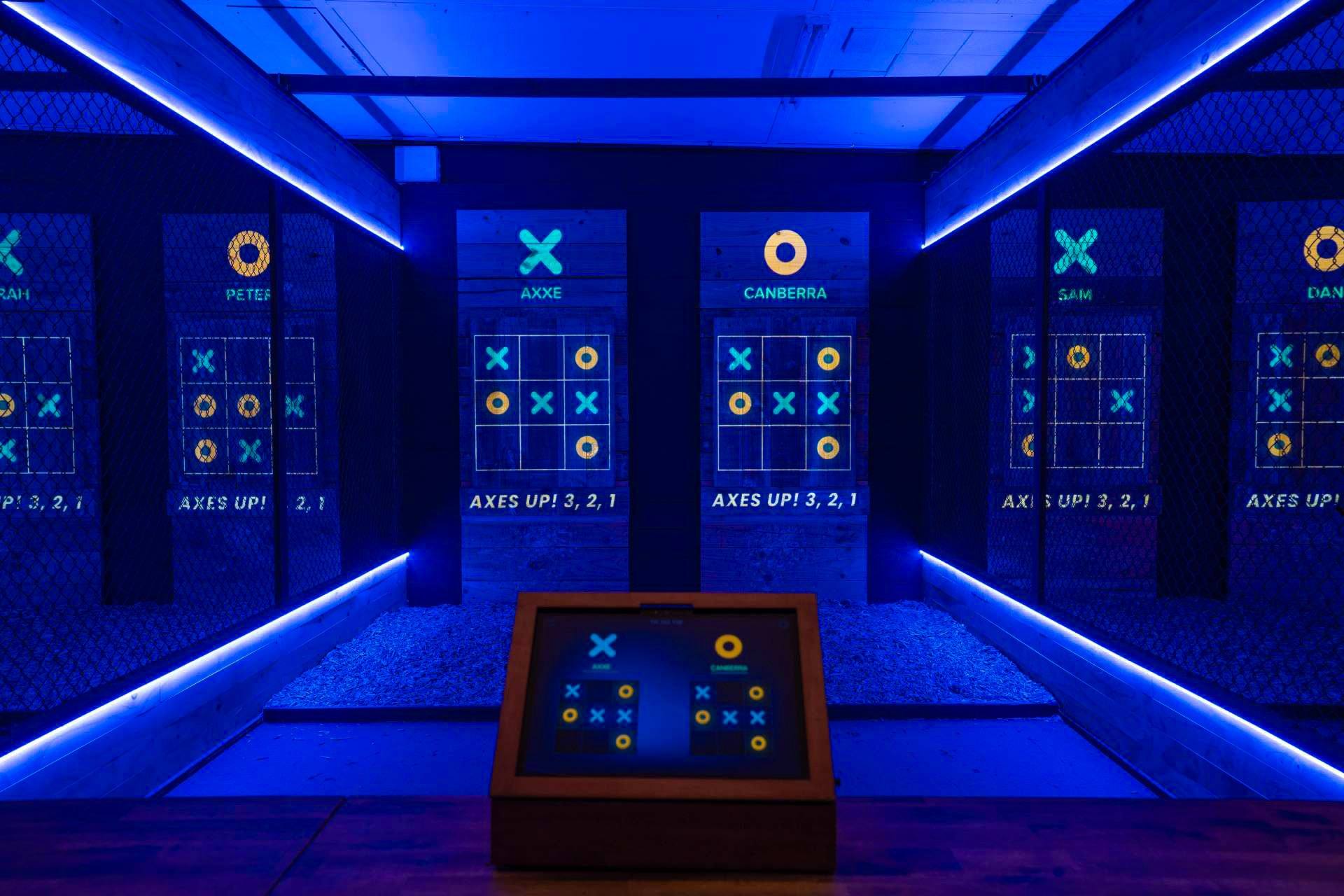 Digital tic-tac-toe grids projected onto axe throwing targets in blue light