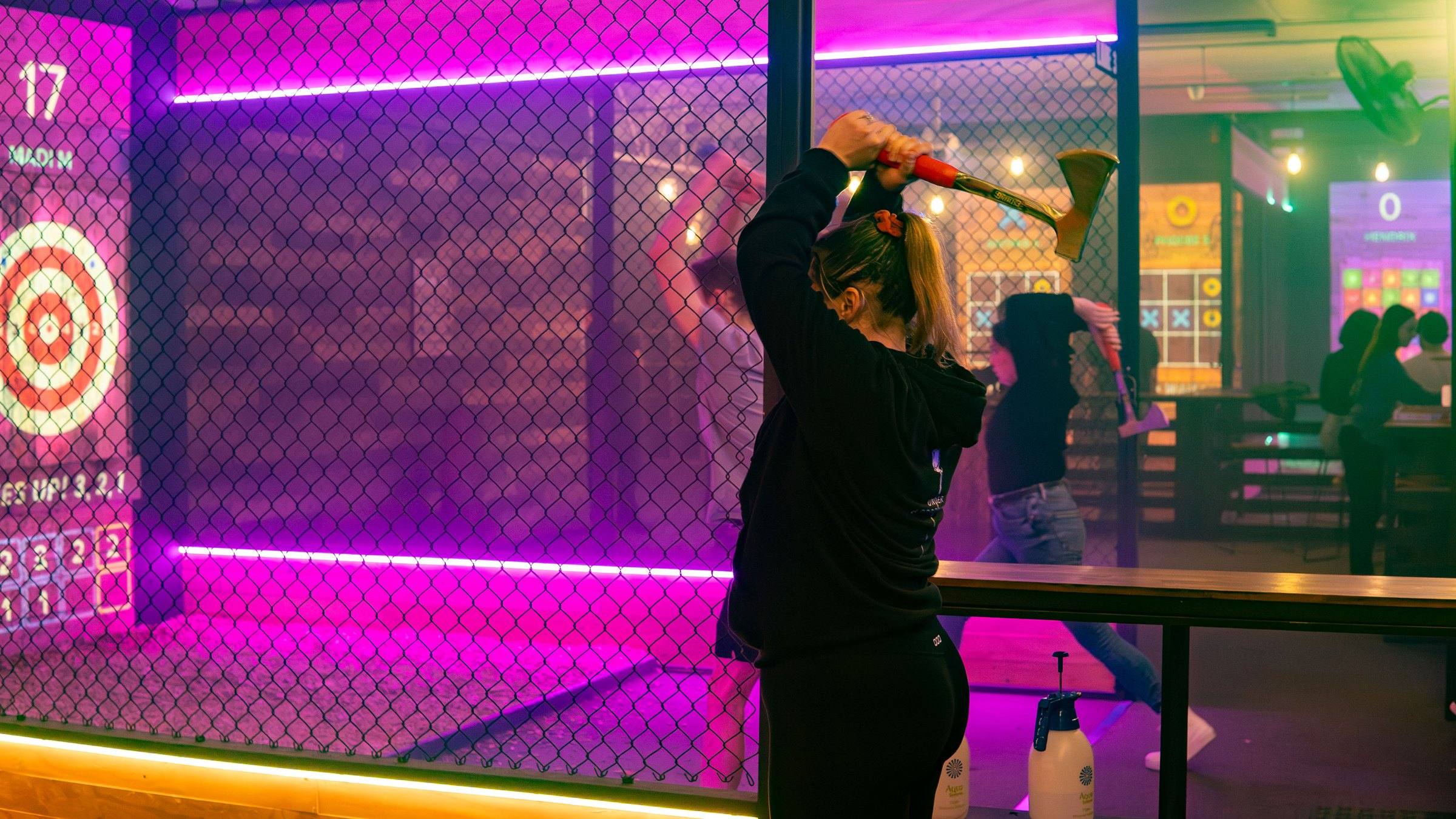 Thrower lining up an axe in a pink-lit lane