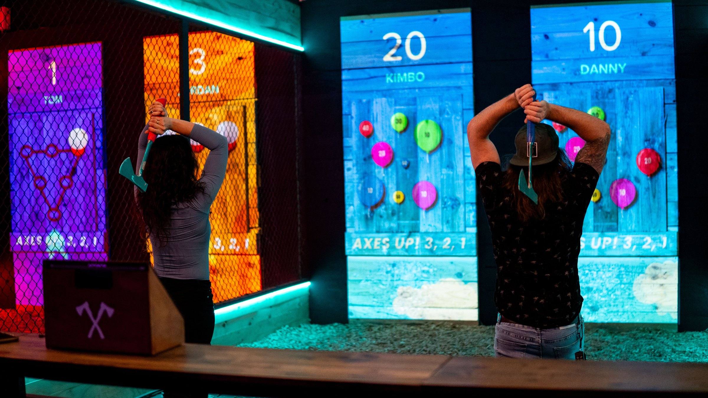 Two people throwing axes at digital balloon targets with live scores